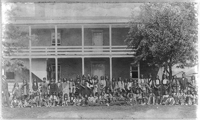 Image shows a large group of Sioux boys posed in front of a school building