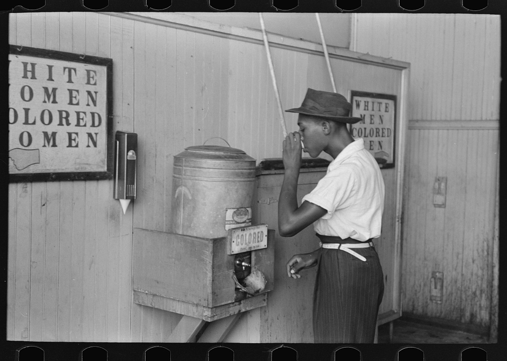 Image shows a Black person drinking at a "Colored" water cooler in a streetcar terminal in Oklahoma City, Oklahoma