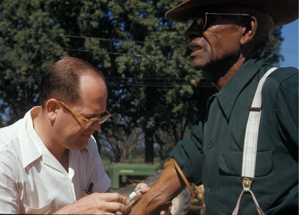 Image shows a researcher collecting a blood sample from a subject as part of the USPHS Untreated Syphilis Study and Tuskegee
