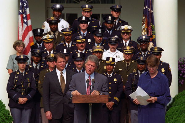 Image shows President Clinton delivering his Anti-Crime Initiative announcement surrounded by the vice president, attorney general, and law enforcement members