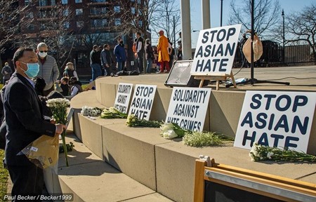 Image shows people placing flowers in front of a display of posters that say "Stop Asian Hate"