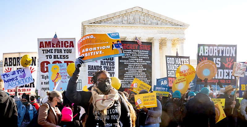 Image shows a crowd of people holding signs and protesting outside the Supreme Court during the Dobbs v. Jackson case