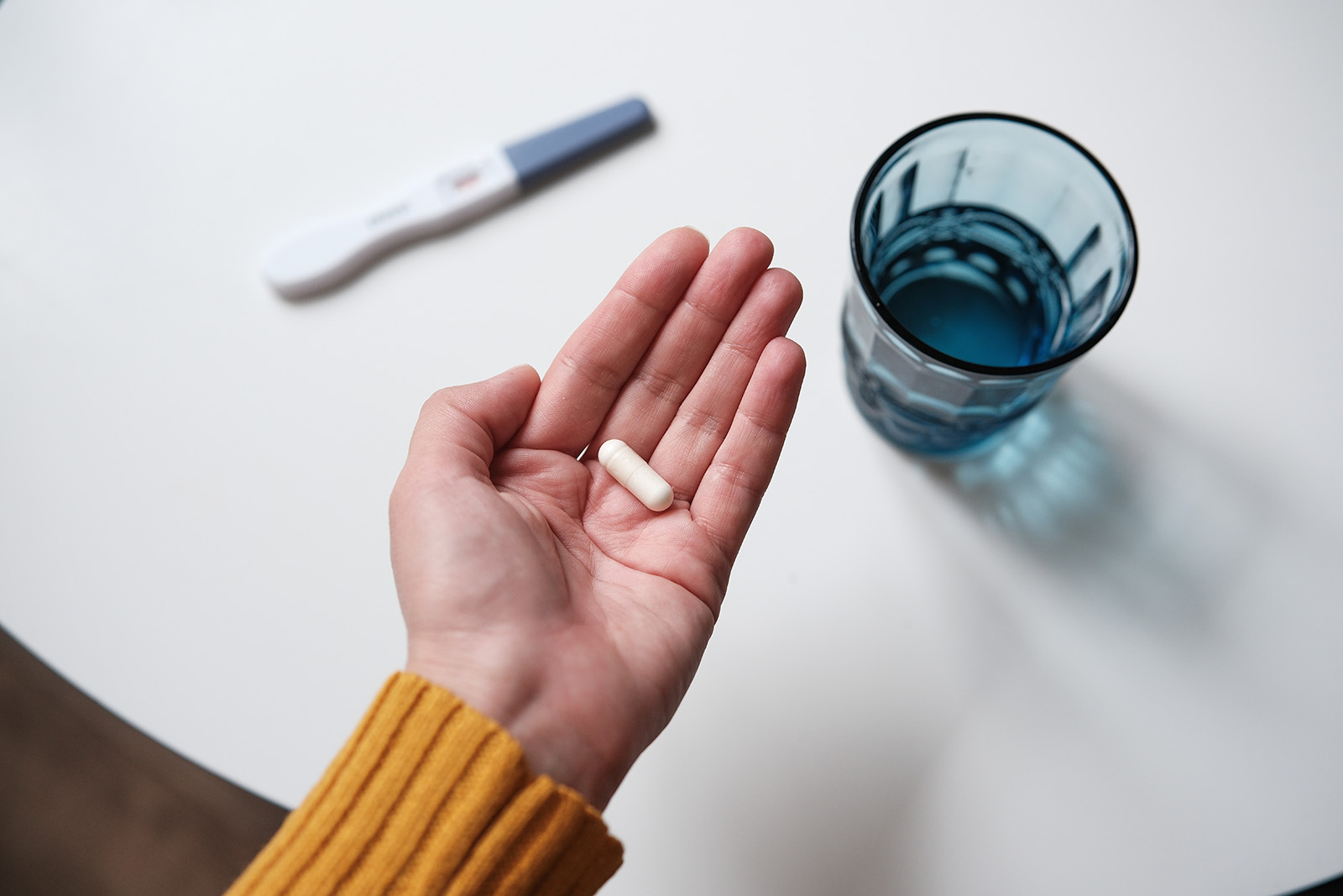 Image of a person holding a pill next to a glass of water and a thermometer