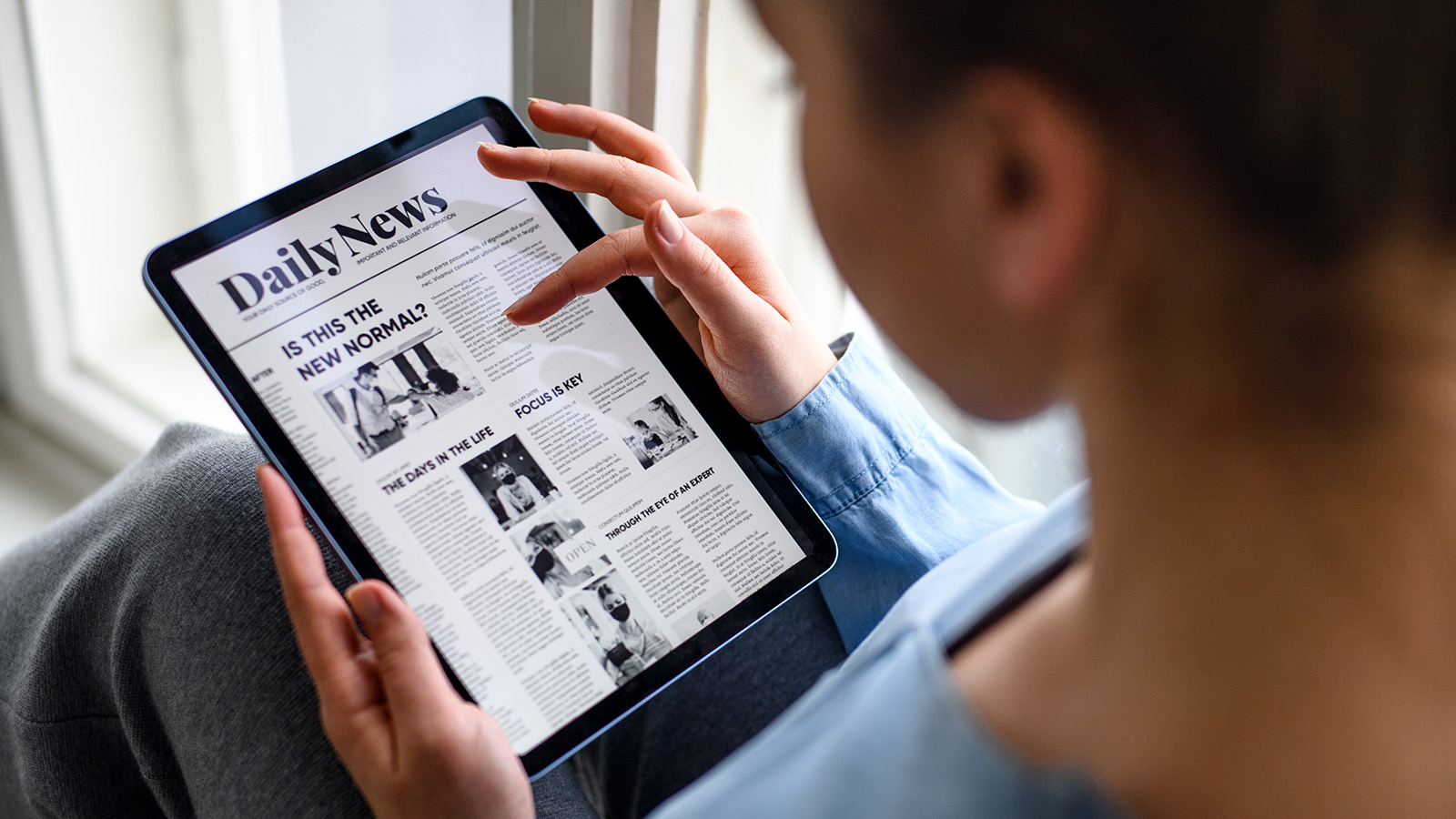 A photograph of a person scrolling through a news web site on a tablet