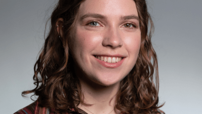 Photo of Abby Sachar in an red-earth-toned striped button down against a gray background