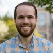 Photo of Joel Luther in a plaid shirt with trees and a building in the background