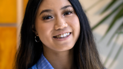 Photo of Julianne Wong in a light blue pinstripe button up against an office wall adorned with a plant and golden canvases.