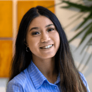 Photo of Julianne Wong in a light blue pinstripe button up against an office wall adorned with a plant and golden canvases.