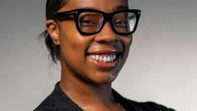 Headshot photo of Natiya Clark in a black top and black glasses against a gray background.