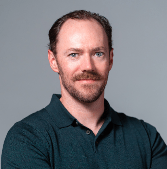 Professional photo of Zach Dyer wearing a colored dark teal shirt against a gray background.