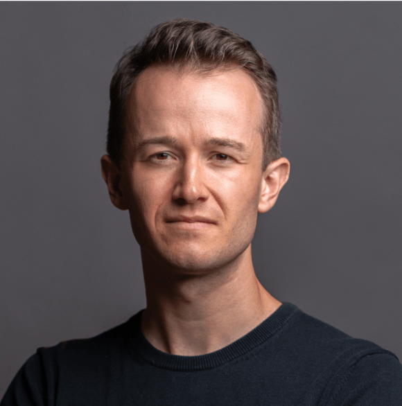 Professional headshot photo of Gabe Brizon-Trezise in a black shirt against a gray background.