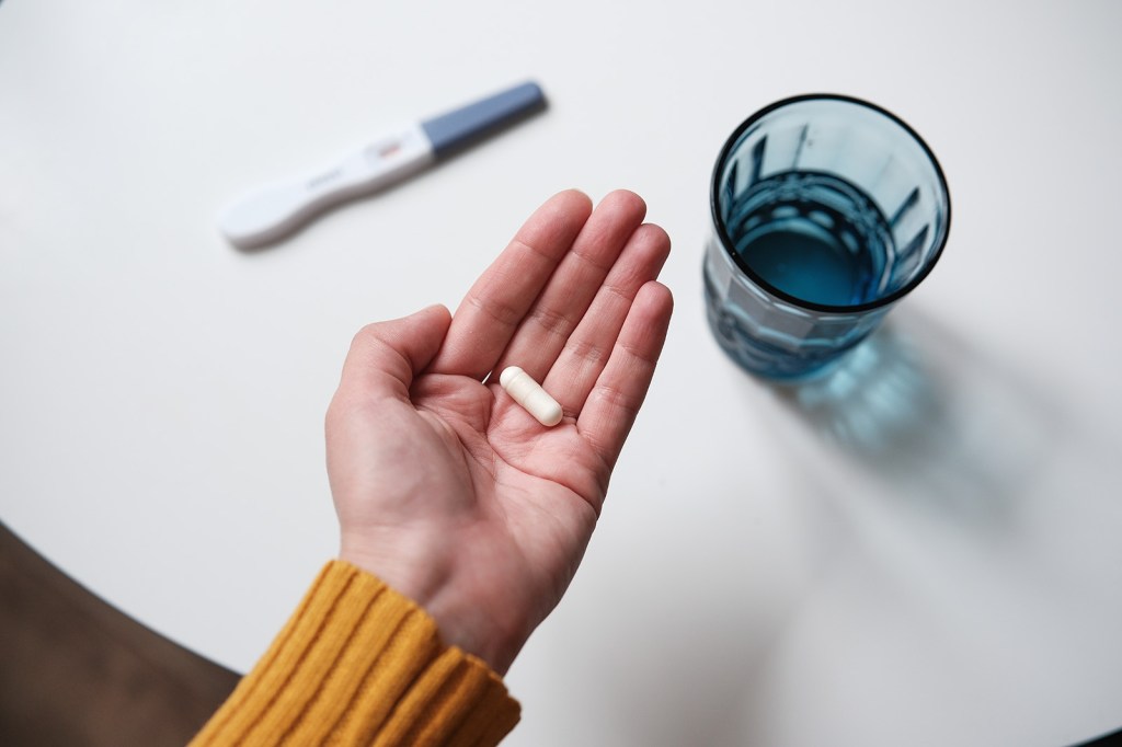 Image of a person holding a pill next to a glass of water and a thermometer