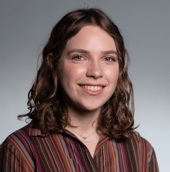 Photo of Abby Sachar in an red-earth-toned striped button down against a gray background