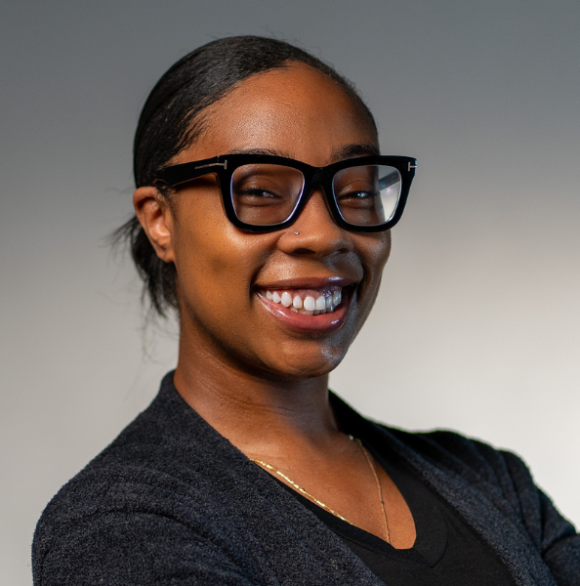 Headshot photo of Natiya Clark in a black top and black glasses against a gray background.