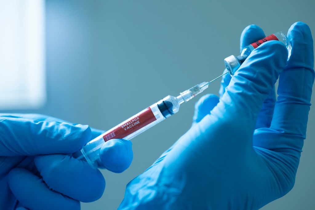 Gloved hands draw small pox vaccine into a syringe.