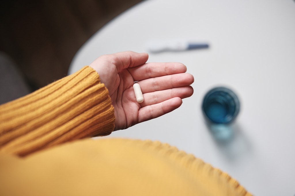 Photo of a person in a yellow sweater holding a capsule in their hand