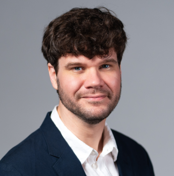 Professional headshot of Andrew Jones wearing a white collared shirt with a blue suit jacket against a gray background.