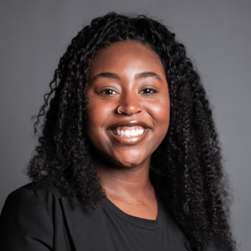 Professional headshot of Briah Lumpkins smiling in a black shirt against a gray background.