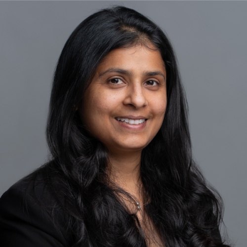 Professional photo of Avni Gupta smiling in a black blazer against a gray background.