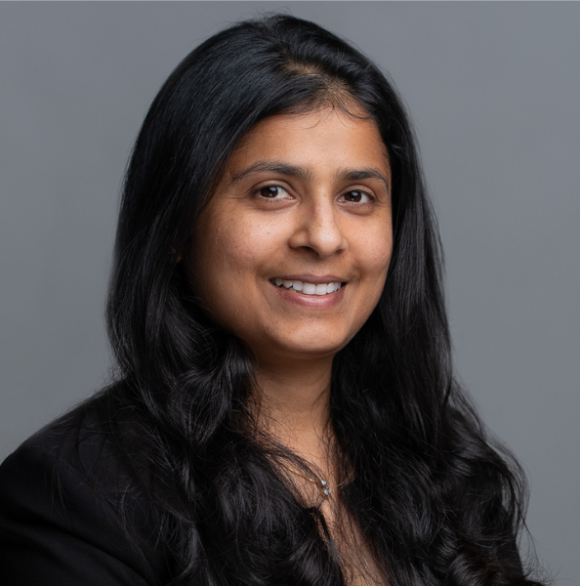Professional photo of Avni Gupta smiling in a black blazer against a gray background.