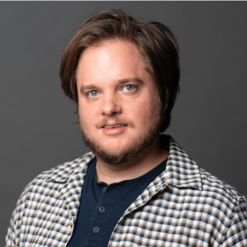 Professional head shot photo of Charles Harpole in a checkered button up against a dark gray background.