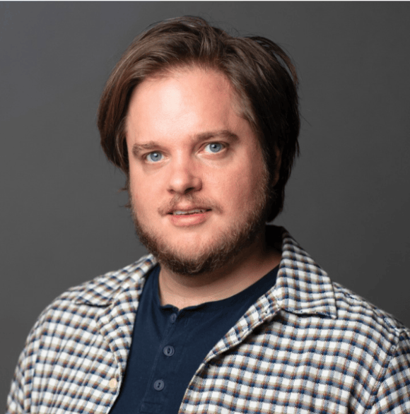 Professional head shot photo of Charles Harpole in a checkered button up against a dark gray background.